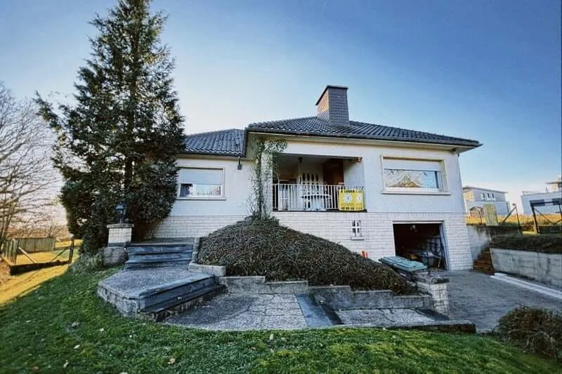 A YWS shared house in Luxembourg: a white house with a dark tiled roof, a lawn and a fir tree